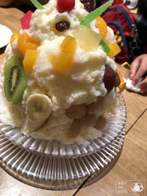 Kagoshima's famous shaved ice: a big bowl of shave dice with condensed milk and many pieces of fruits: kiwi, banana, mandarins, cherries, even beans and sweet potato