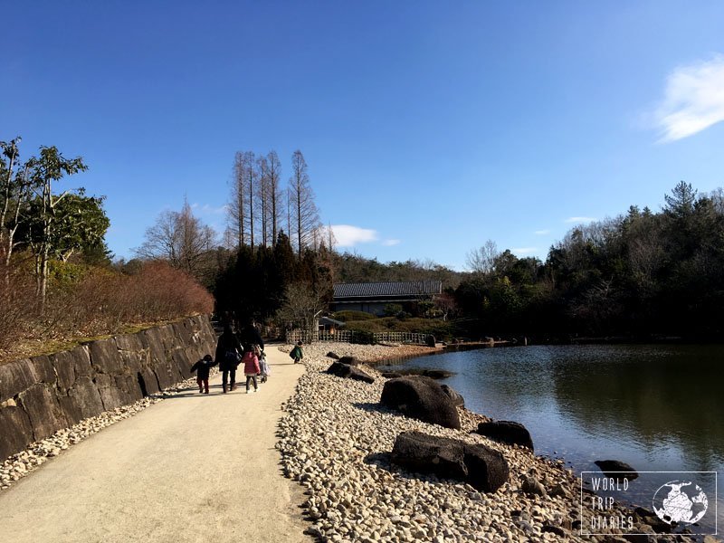 A path beside a lake with wintery plants and a family walking on it. The path to the house from My Neighbor Totoro is just as lovely!