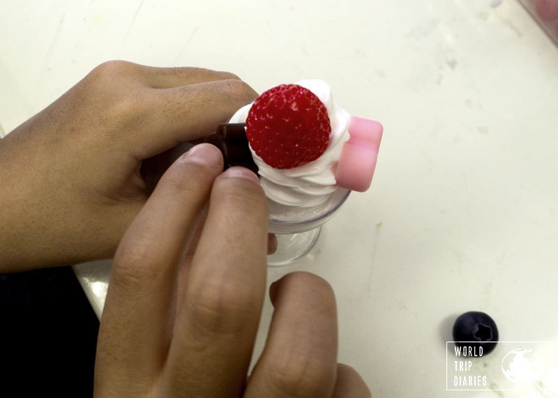 One of the kids' hands placing a decoration on the plastic ice cream Sunday - best workshop for families in Tokyo, Japan!