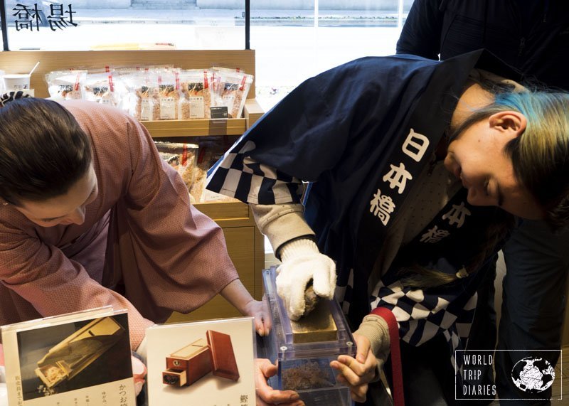 Kid-1 trying to make bonito flakes our of a dried bonito piece with the help of our guide of the Gourmet Tours in Japan!