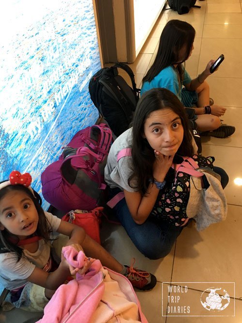 3 of the 4 kids sitting on the airport floor, waiting. Flying (and traveling, in general) means long waits. Be prepared for it!