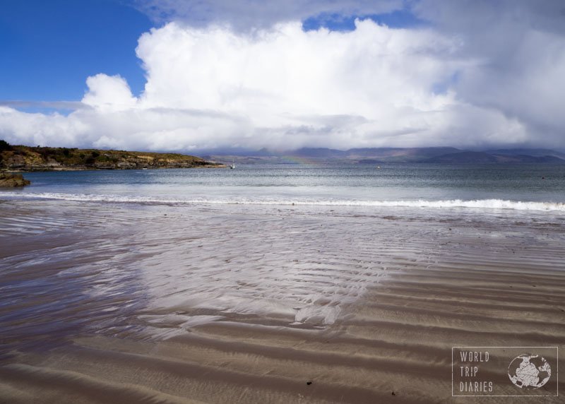 The beach water reflecting the clouds on a thin layer of water over the ripply sand. There's a rainbow at the back, can you see it? Ireland rainbow!