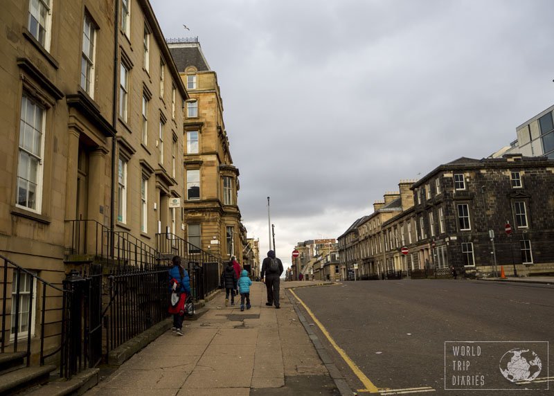 The dad and the kids walking on a street in Glasgow, Scotland, with its buildings around. Glasgow is very walkable and it's delightful! 