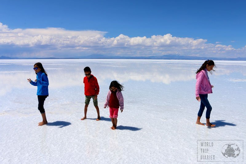 4 kids walking on the salt flats in Bolivia. The white floor is reflecting the clouds. The dreamiest place in the whole world!